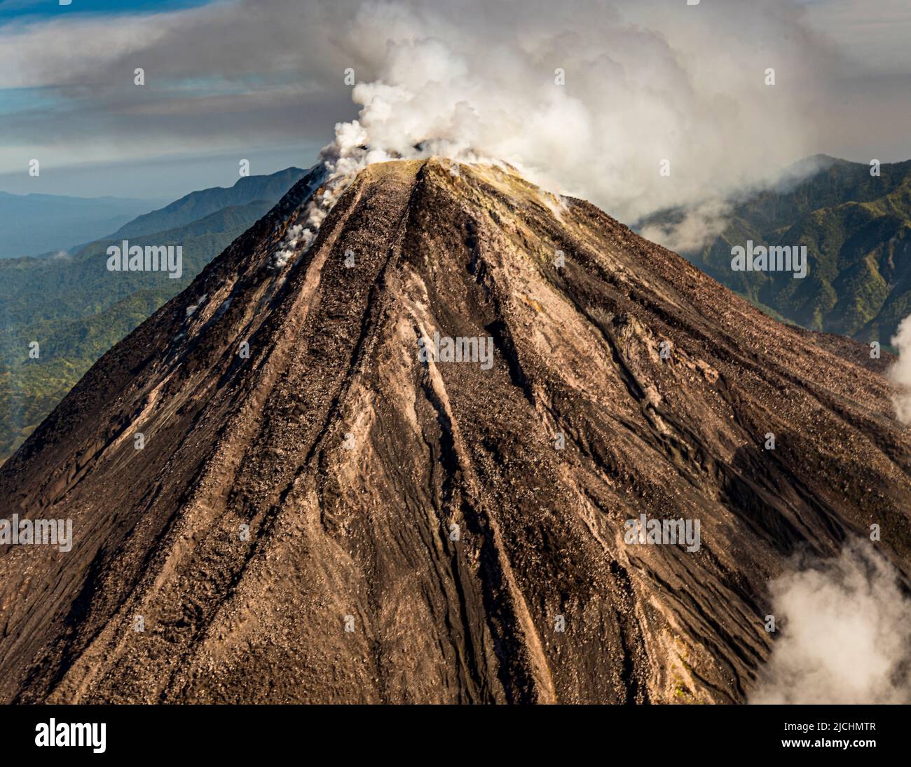 As we approach from the air, the Bagana volcano in Papua New Guinea emits clouds of smoke Stock Photo