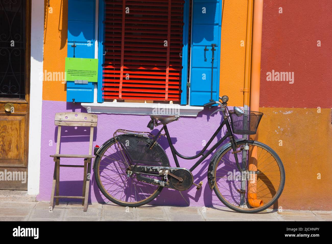 Old Bicycle and Chair leaning against a colorfully painted wall, island of Burano, Venice, Veneto, Italy Stock Photo
