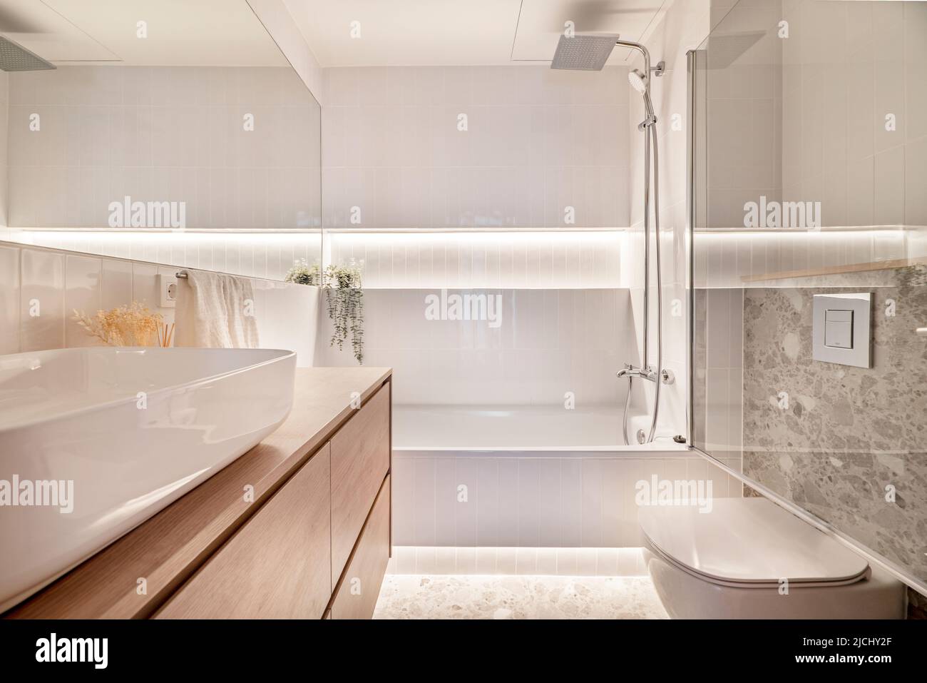 Modern design bathroom with white porcelain sanitaryware, wooden furniture, white porcelain sink, rectangular frameless mirror, bathtub with glass par Stock Photo
