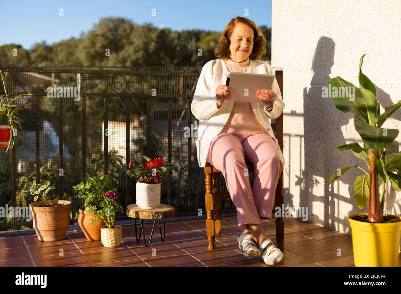 Elderly Caucasian woman using a digital device on the terrace of her house. Concept of technology, communications and senior citizens. Space for text. Stock Photo