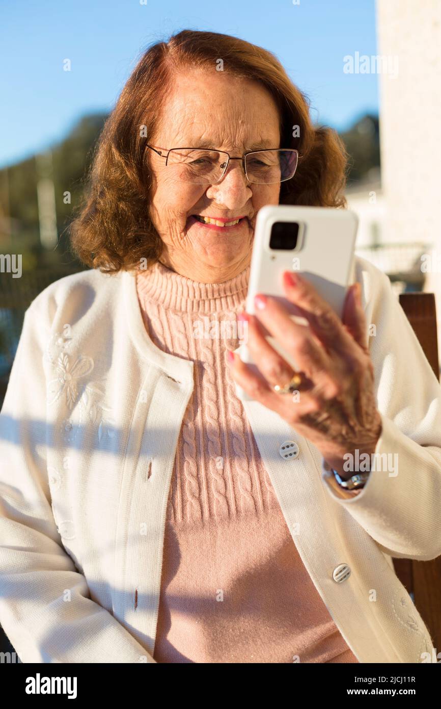 Portrait of smiling Caucasian older woman making a video call through mobile phone. She is outdoors. Stock Photo