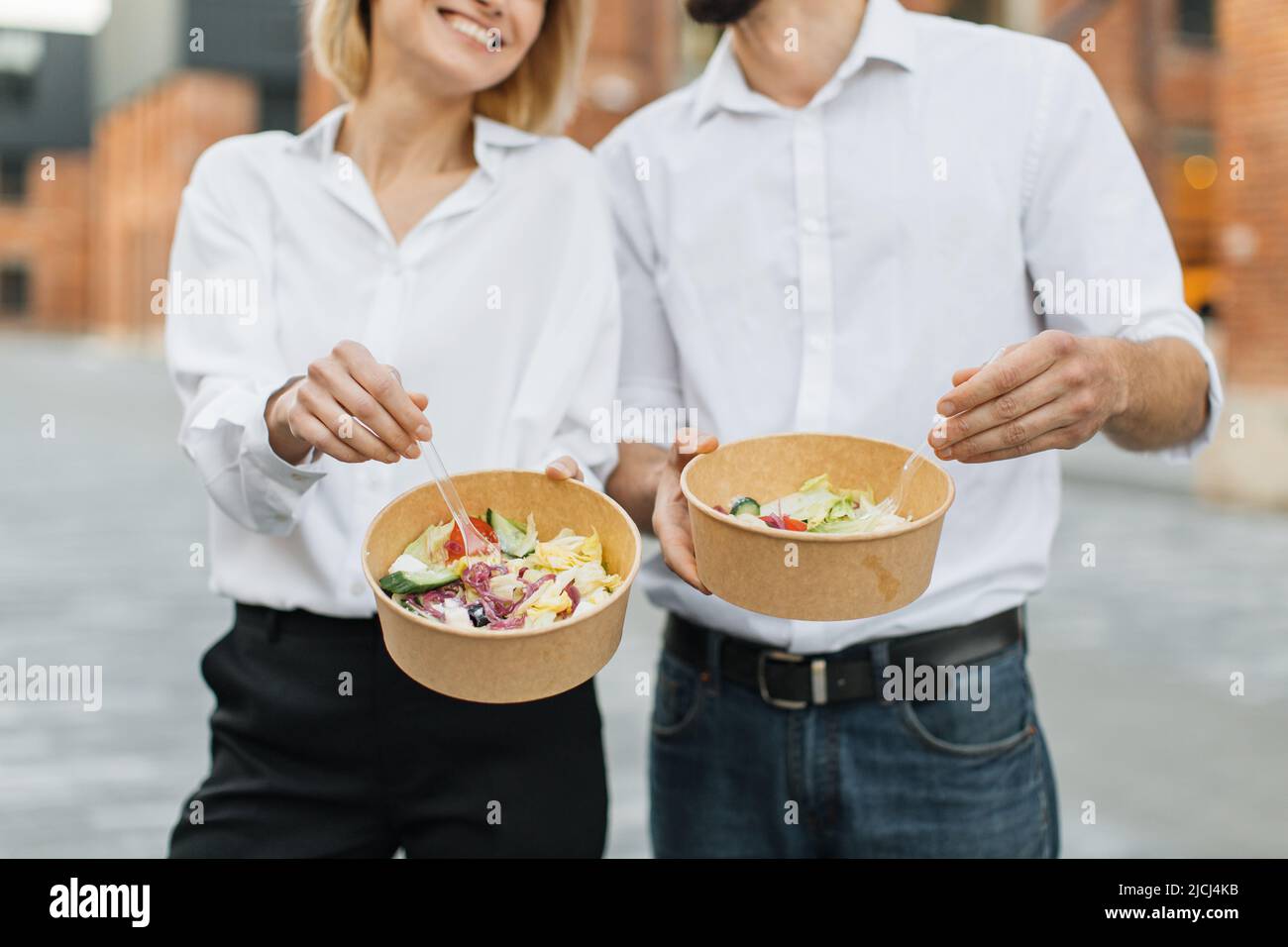 Cropped image of friends, business partners, caucasian man and woman with organic salad in cardboard bowl. Concept of healthy eating. Stock Photo