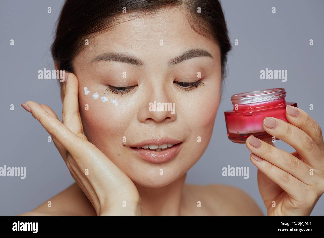 modern asian female with facial cream jar and eye cream on face against