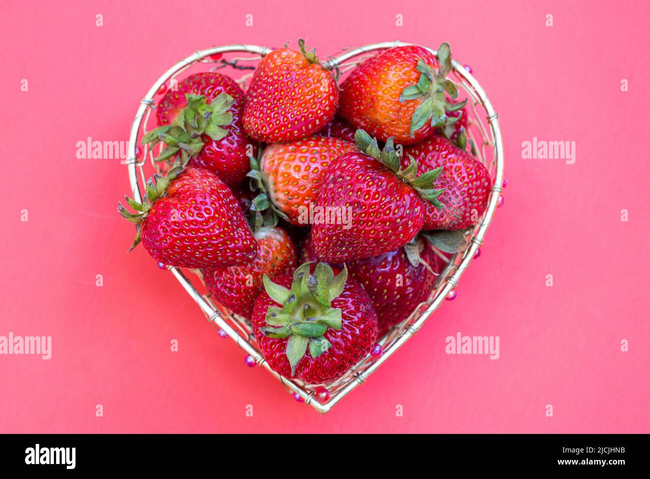Bright red strawberries in a heart shaped wire basket on a white background Stock Photo