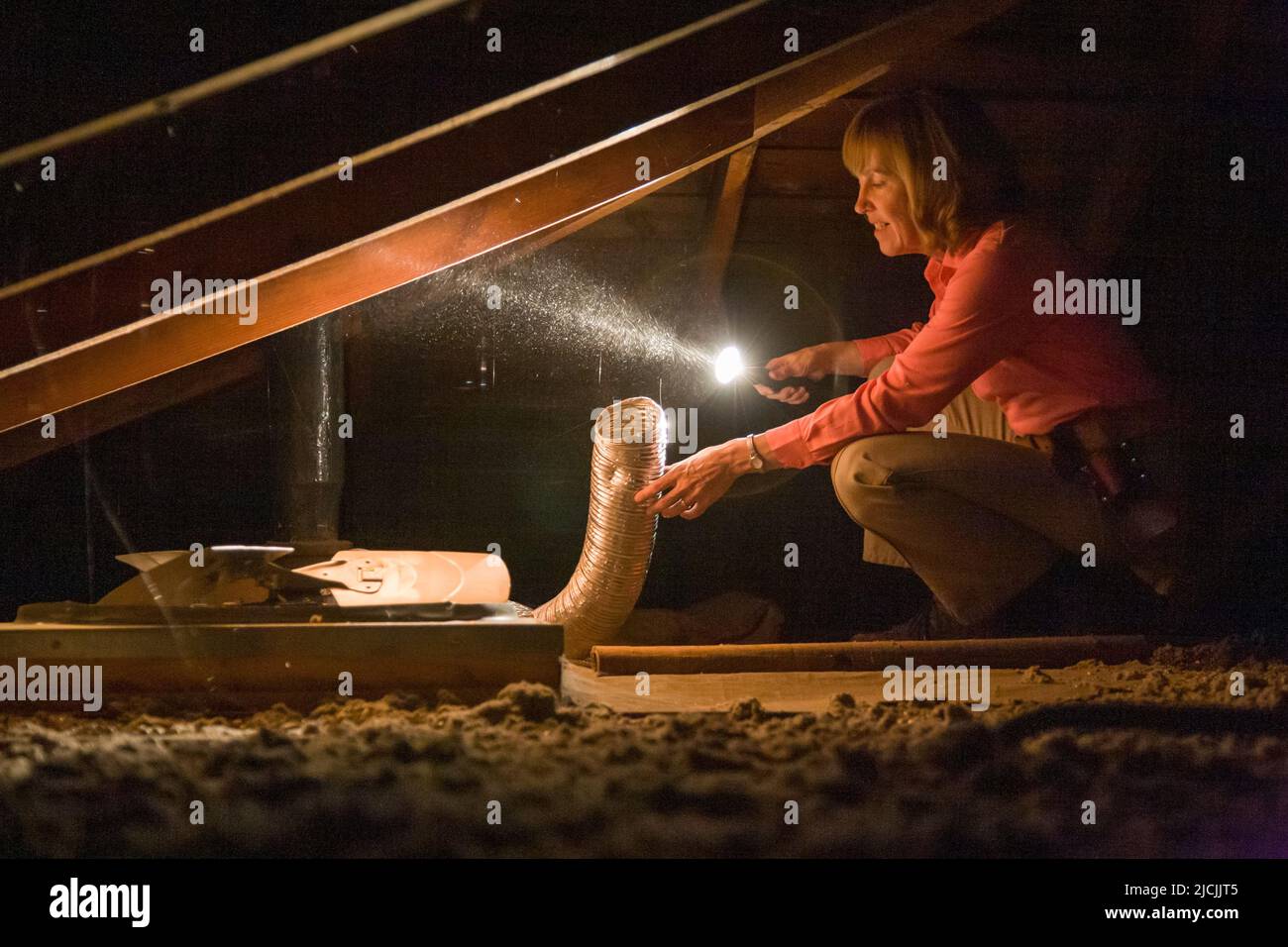 Home inspector in attic with flashlight examining exhaust fan duct. Stock Photo