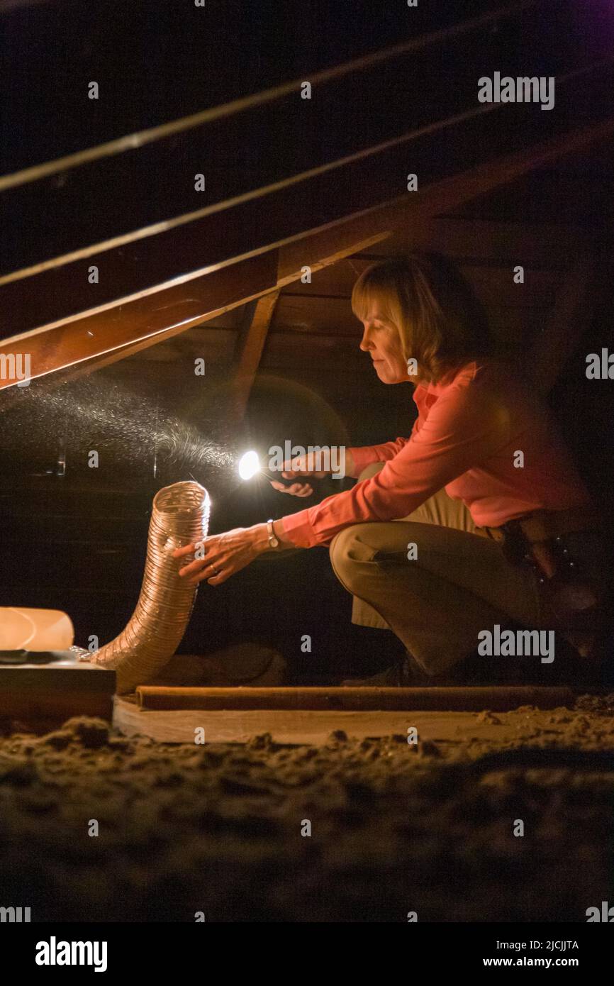 Home inspector in attic with flashlight examining exhaust fan duct. Stock Photo