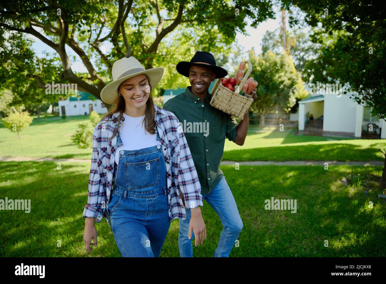 Mixed race farmer friends walking through green fields with vegetable basket Stock Photo