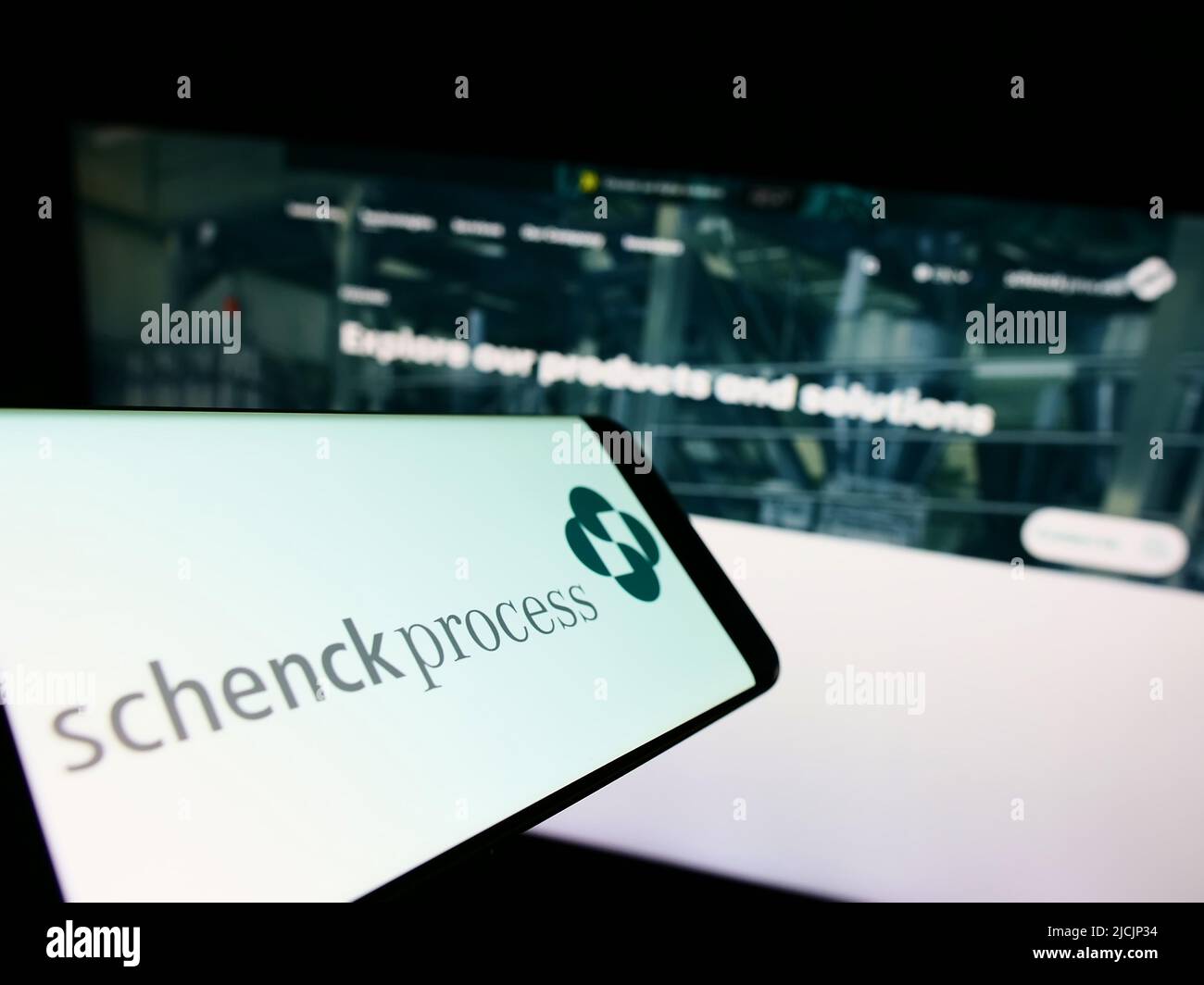 Mobile phone with logo of German company Schenck Process Europe GmbH on screen in front of website. Focus on center-right of phone display. Stock Photo