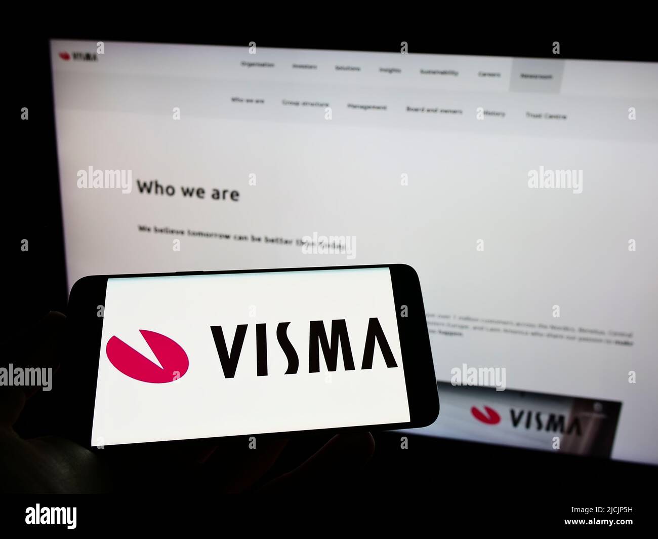 Person holding mobile phone with logo of Norwegian software company Visma AS on screen in front of business web page. Focus on phone display. Stock Photo