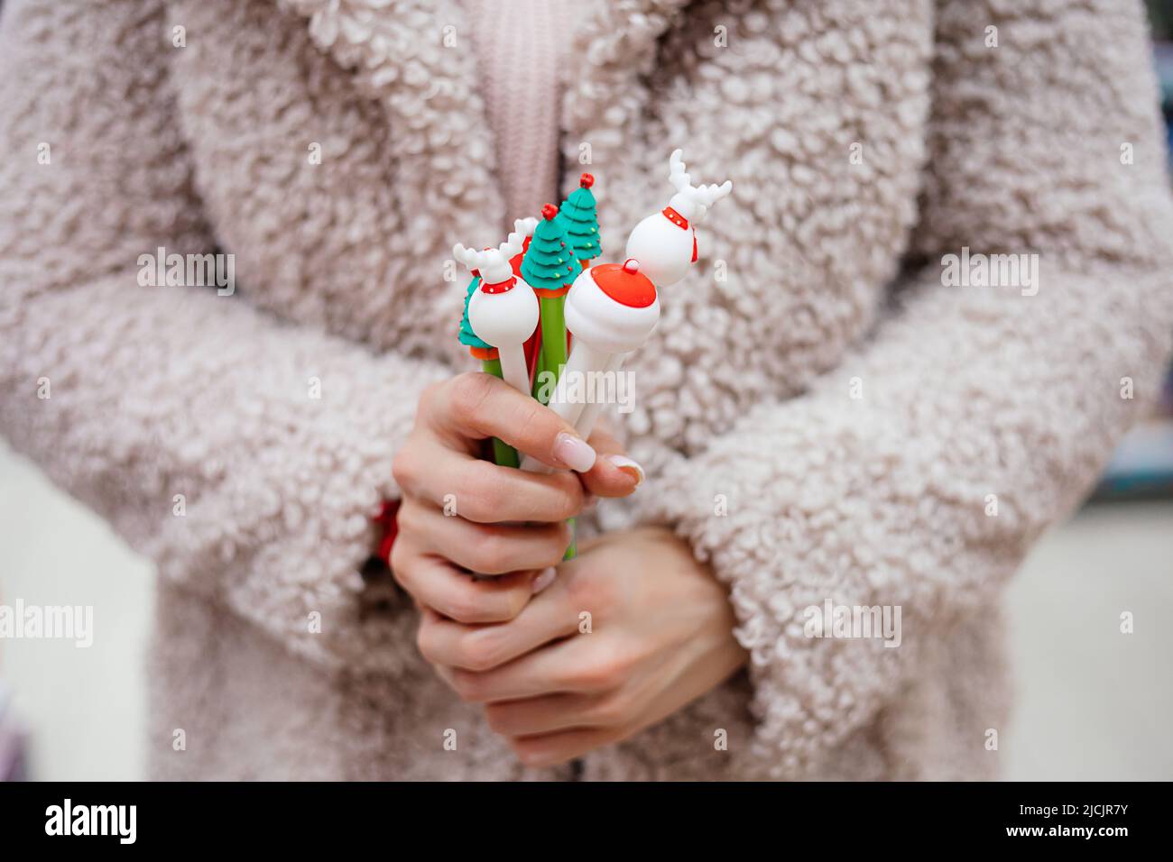 Woman in white coat holds in her hands lot of funny pens for New Year's gifts and surprises. New Year and Christmas. Holiday shopping. Christmas mood Stock Photo
