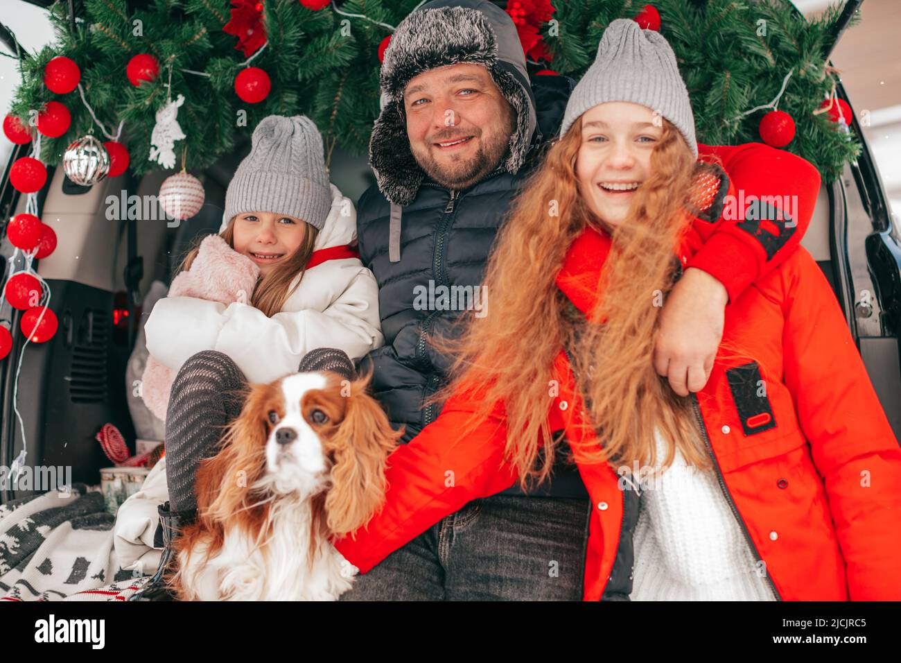 Fatherhood concept. Happy Caucasian family have new year's party outside, red decoration in car trunk, christmas balls. friendly cavalier king charles Stock Photo
