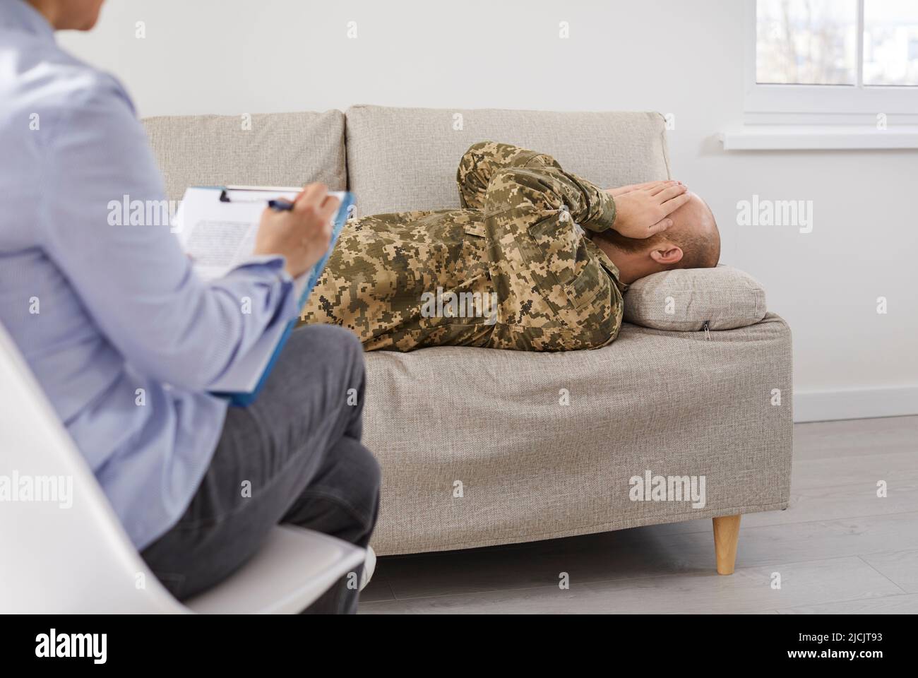 Soldier with military PTSD lying on couch during session with therapist or psychologist Stock Photo