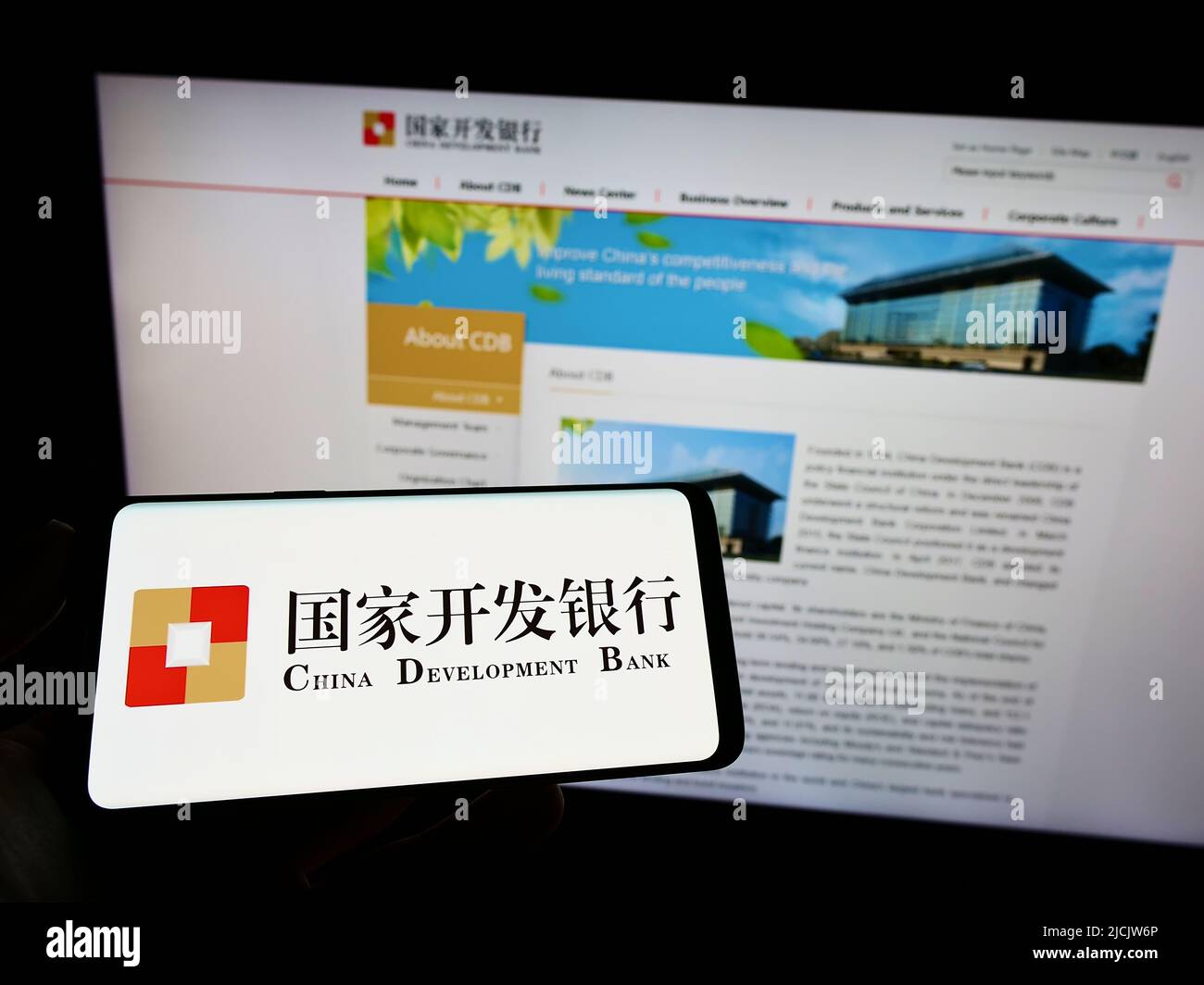 Person holding smartphone with logo of China Development Bank (CDB) on screen in front of website. Focus on phone display. Stock Photo