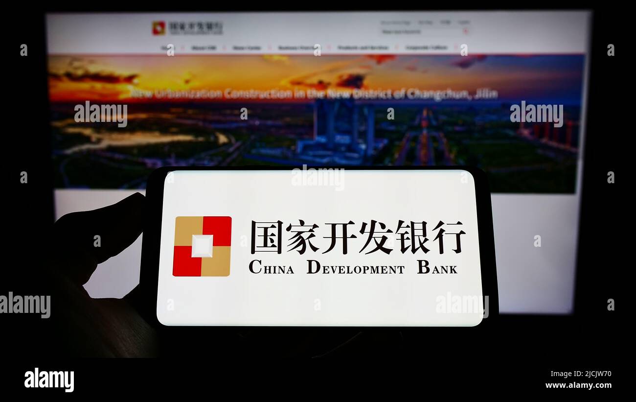Person holding cellphone with logo of China Development Bank (CDB) on screen in front of webpage. Focus on phone display. Stock Photo