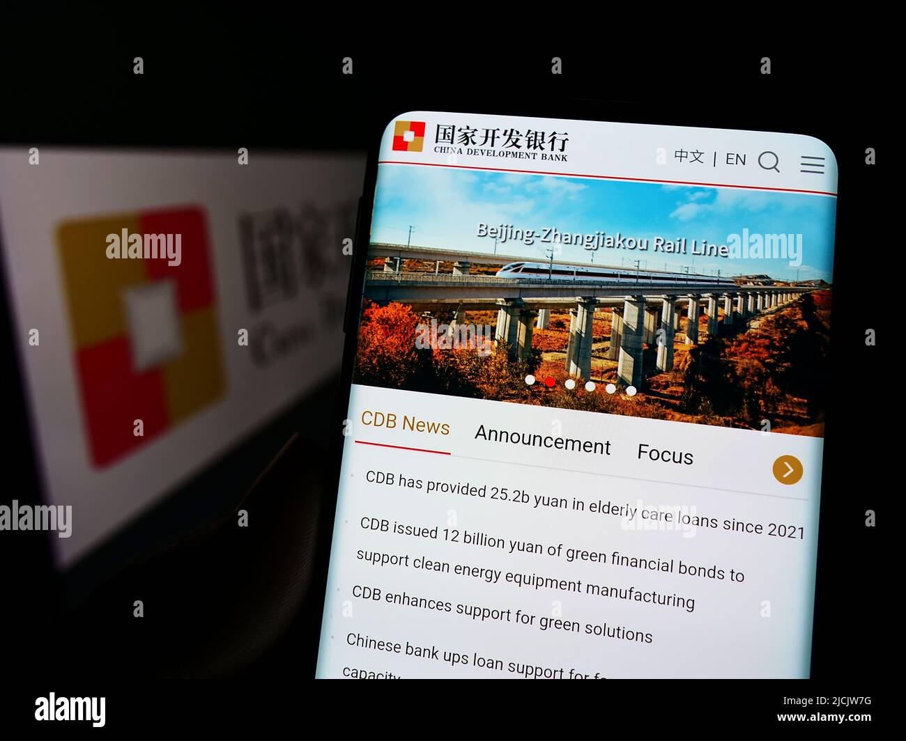 Person holding smartphone with logo of China Development Bank (CDB) on screen in front of website. Focus on phone display. Stock Photo