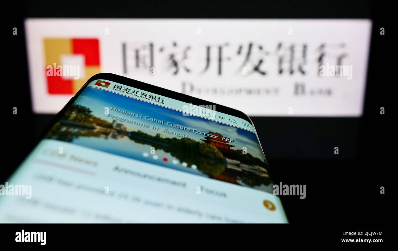 Person holding smartphone with logo of China Development Bank (CDB) on screen in front of website. Focus on phone display. Stock Photo