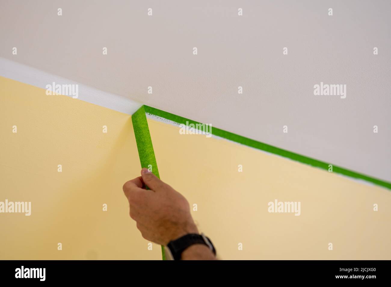 Painter removes masking tape and creates a sharp border between a yellow and white painted part of a wall. Stock Photo