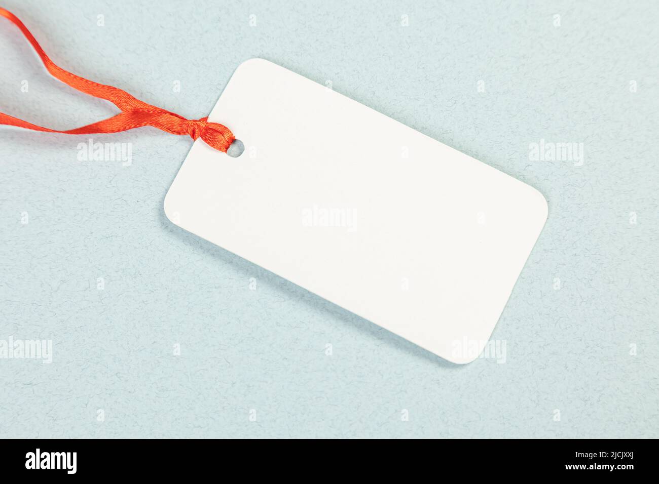 An empty white price tag lies on a gray-blue background with a soft shadow. Stock Photo