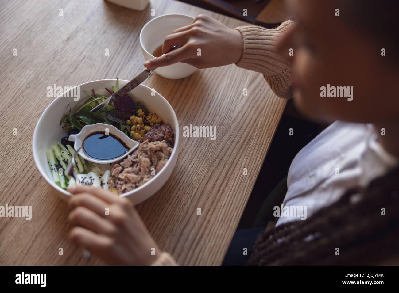 Top view of woman holding cutlery and eating healthy food served in white ceramic bowl at food and drink establishment Stock Photo