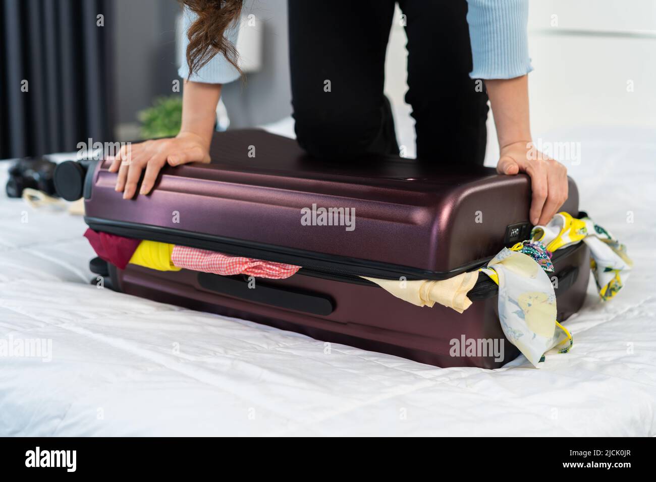woman trying to close overfilled suitcase on her bed Stock Photo