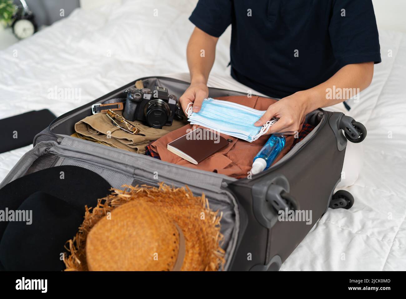man hand packing suitcase luggage including face mask and alcohol spray to protect coronavirus (covid-19) on a bed Stock Photo