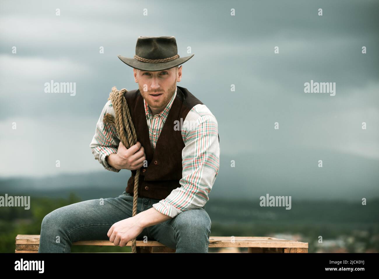 American cowboy man. Handsome brutal western guy. Cowboy with lasso rope on  sky background. Photos