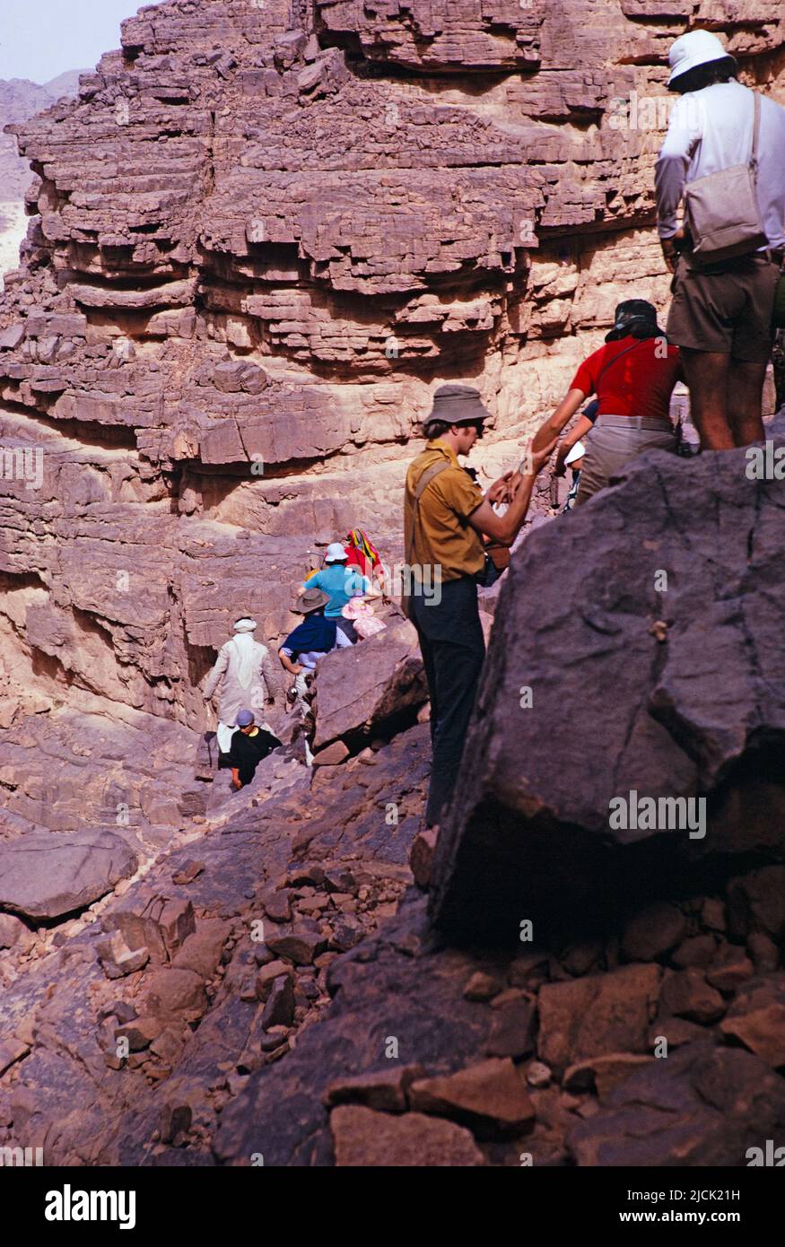Tourists clambering down rocks visiting prehistoric sites, Tassili N'Ajjer National Park, Algeria, north Africa 1973 Stock Photo