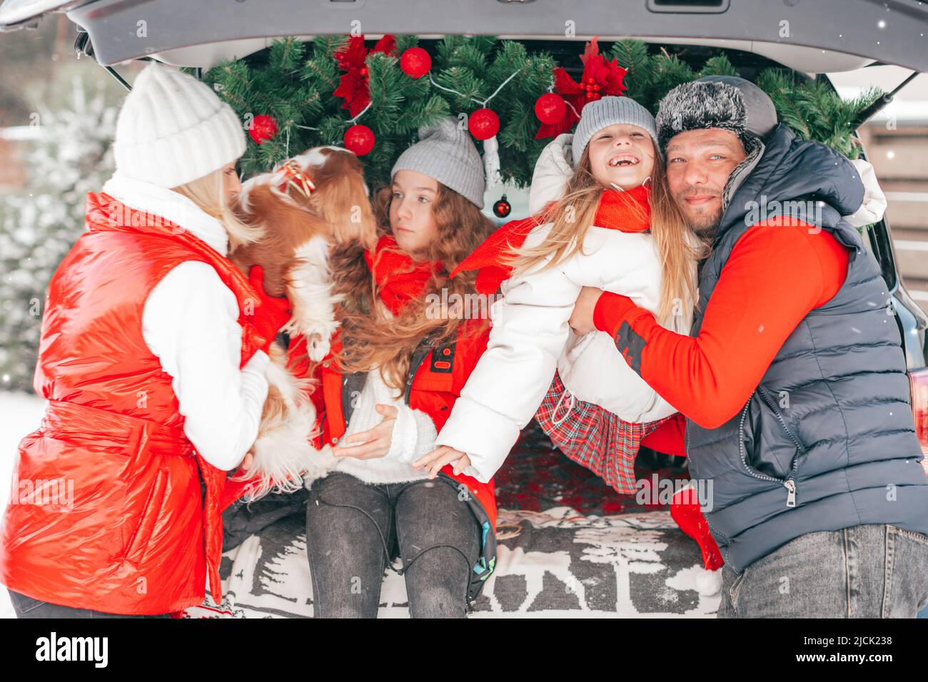 Happy winter moments for family with two children. Father, mother, girls spending time together with dog outdoors in car trunk with red Christmas Stock Photo