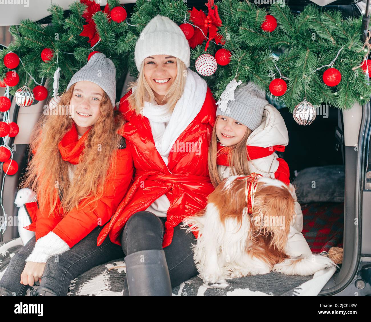 Family celebration New Year or have Christmas party, mother and two daughters in car trunk. Happy friends embracing outdoors Stock Photo