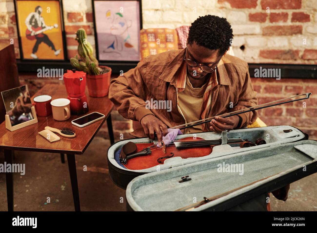 Young black man skilled in playing violin opening slipcover with musical instrument and taking it out while going to perform piece of music Stock Photo