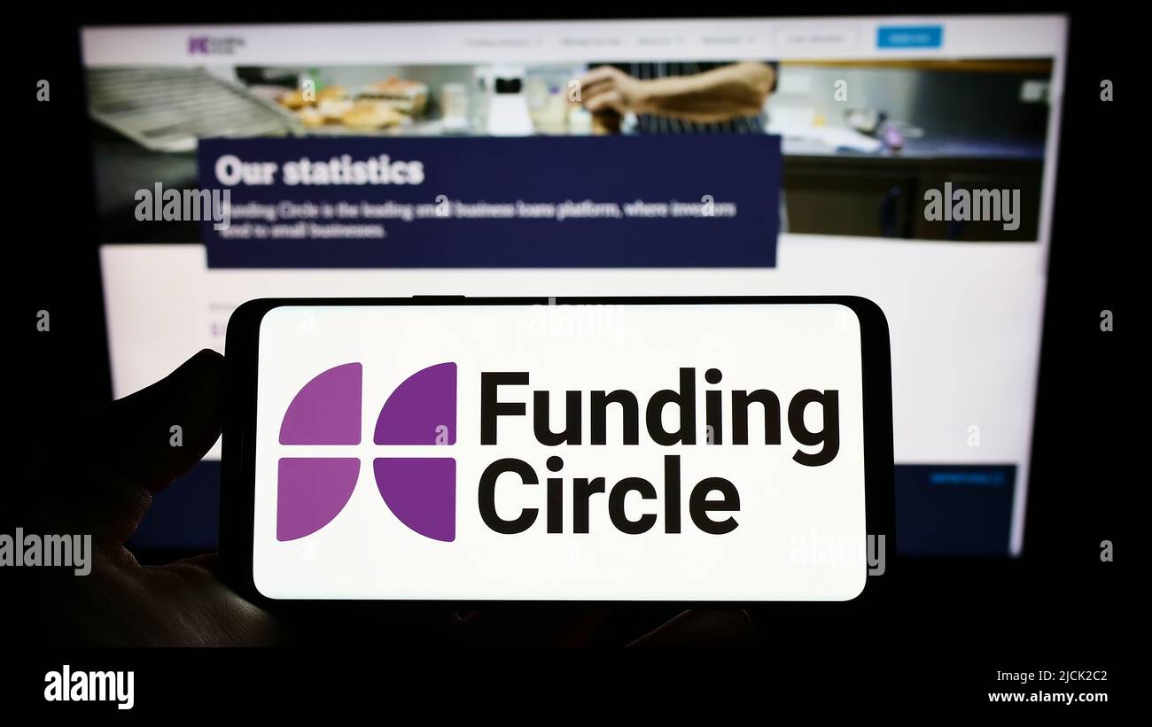 Person holding smartphone with logo of British lending company Funding Circle Ltd. on screen in front of website. Focus on phone display. Stock Photo