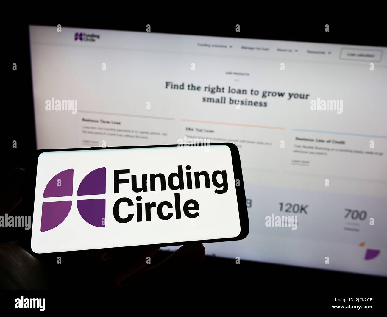 Person holding cellphone with logo of British lending company Funding Circle Ltd. on screen in front of business webpage. Focus on phone display. Stock Photo