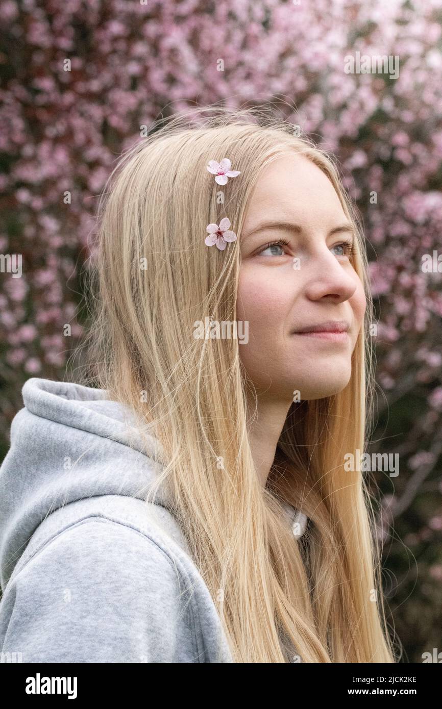 Portrait of a young blonde woman having pink cherry blossom in her hair ...