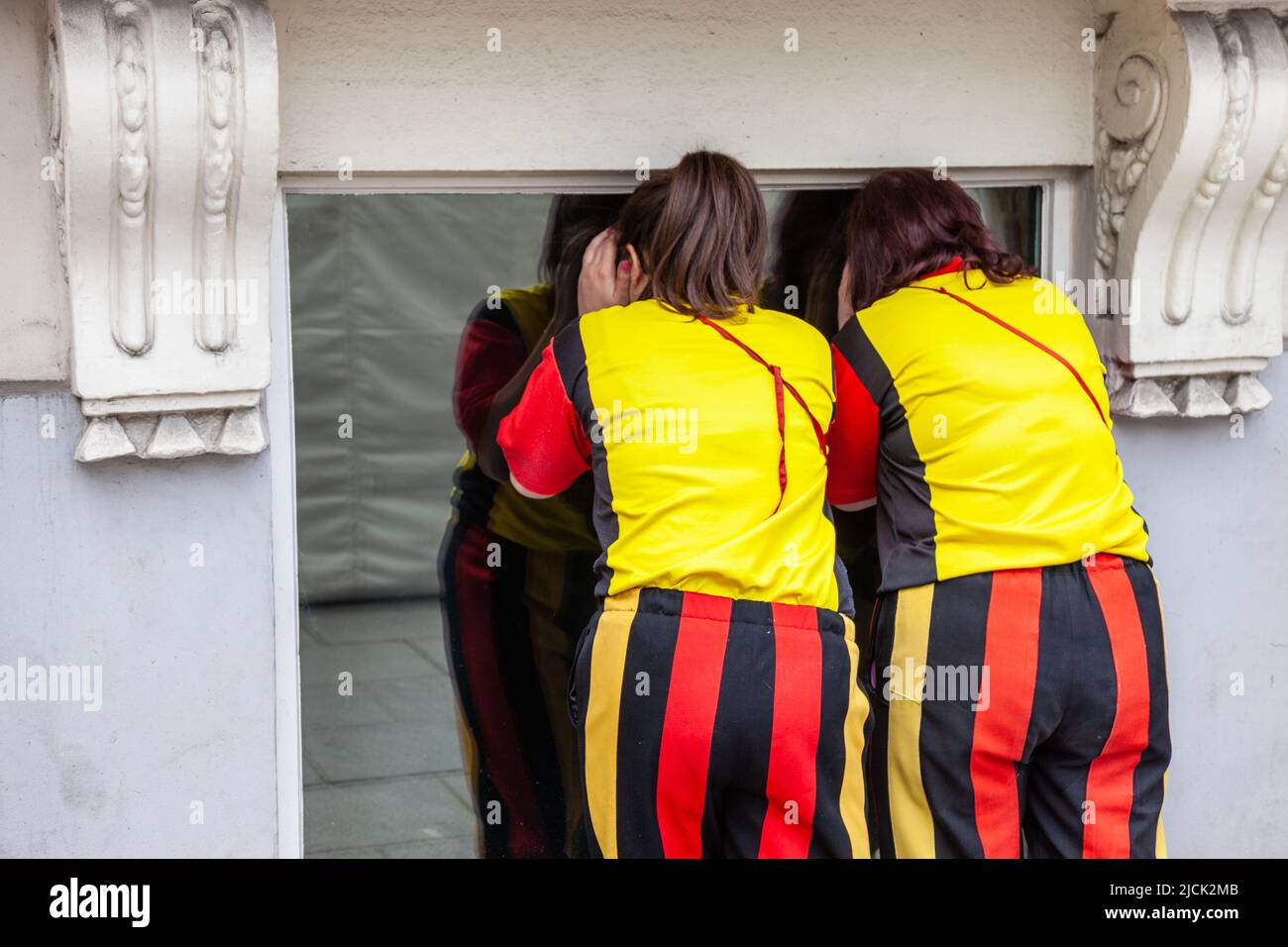 Two women, wearing a costume reminiscent of the colors of Belgium, trying to observe the interior of a building through a window. Brussels. Stock Photo