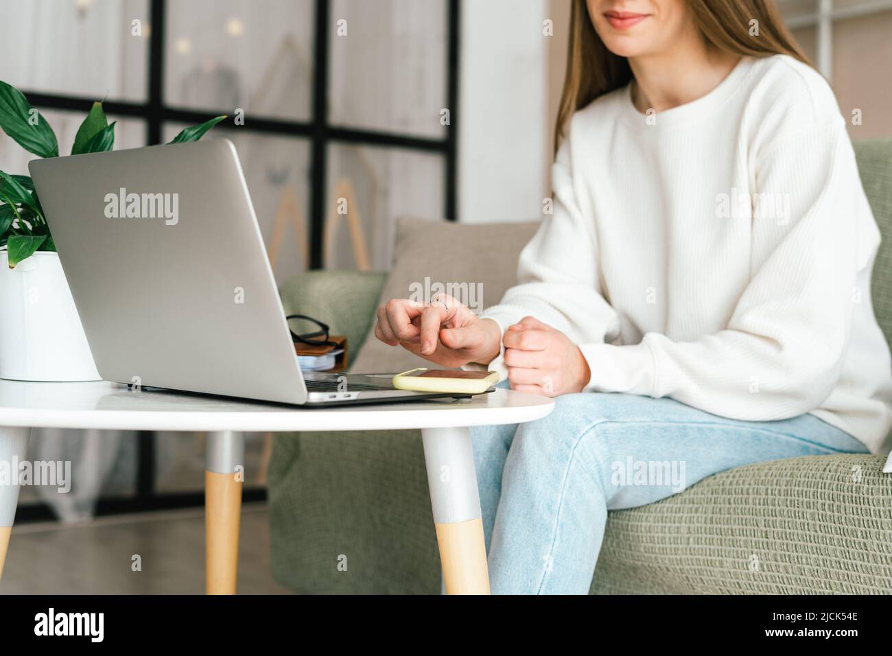 Freelance young woman with mobile cellphone typing at laptop and working from home office with. Happy girl on workplace at desk. Distance learning Stock Photo