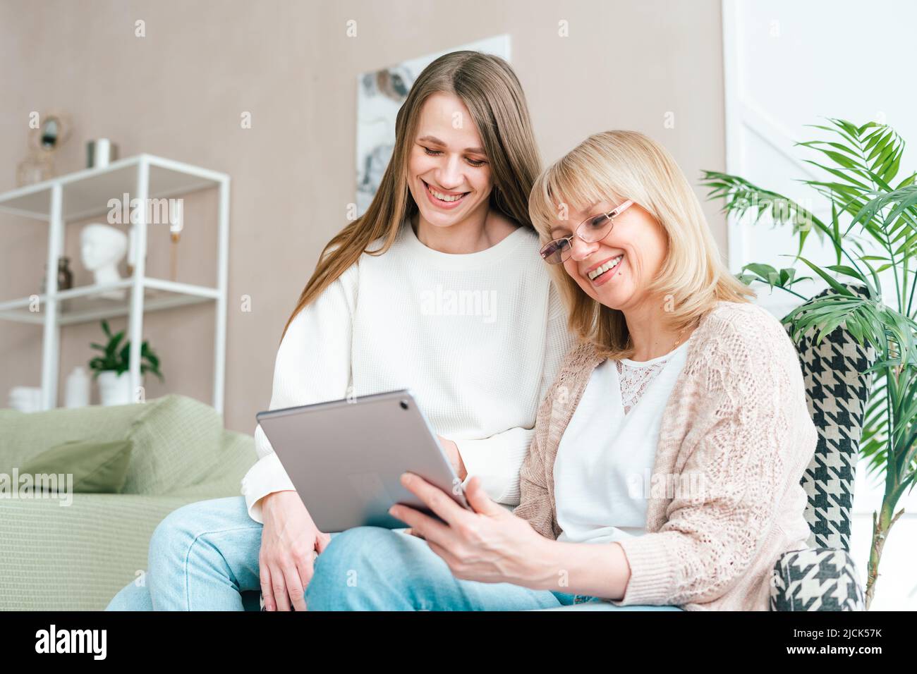 Senior woman and daughter playing with tablet pc. Smiling older woman and her granddaughter sitting home using gadget digital device for online Stock Photo
