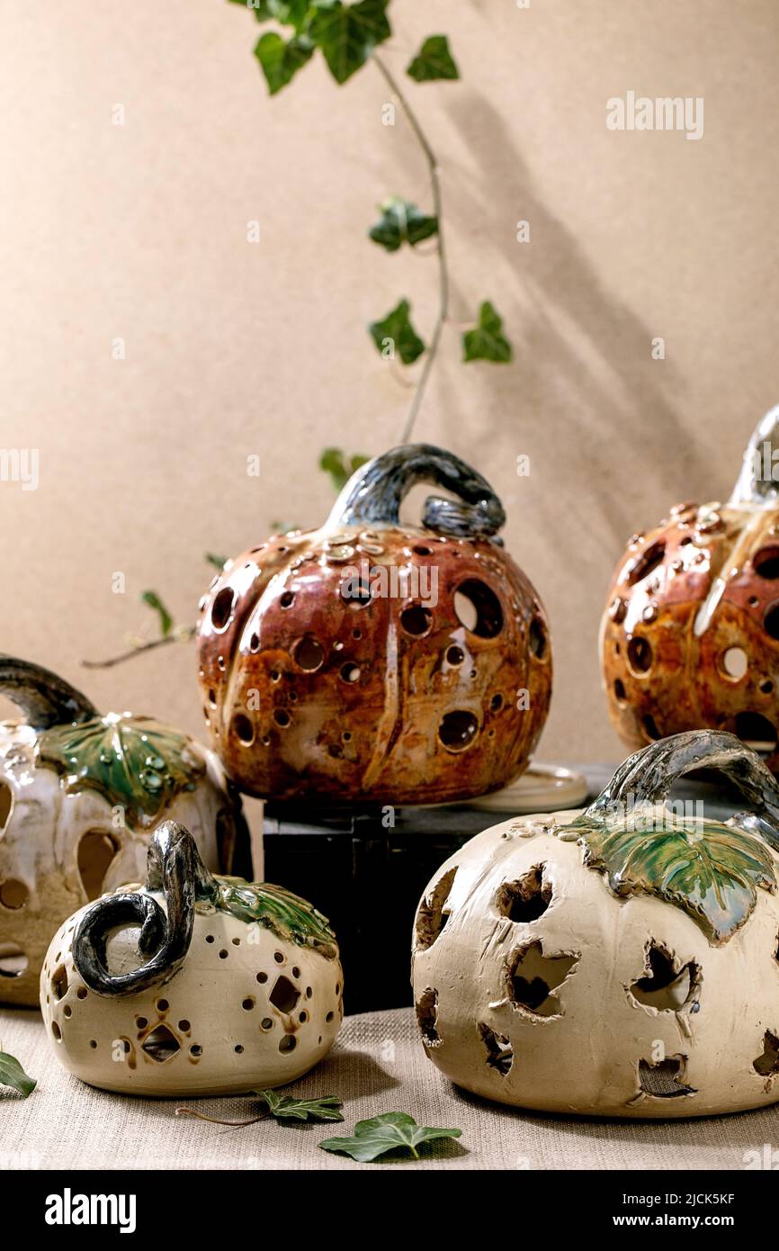 Halloween decorations, set of white and brown handcrafted carved ceramic pumpkins standing on table with ivy leaves. Halloween or Thanksgiving holiday Stock Photo