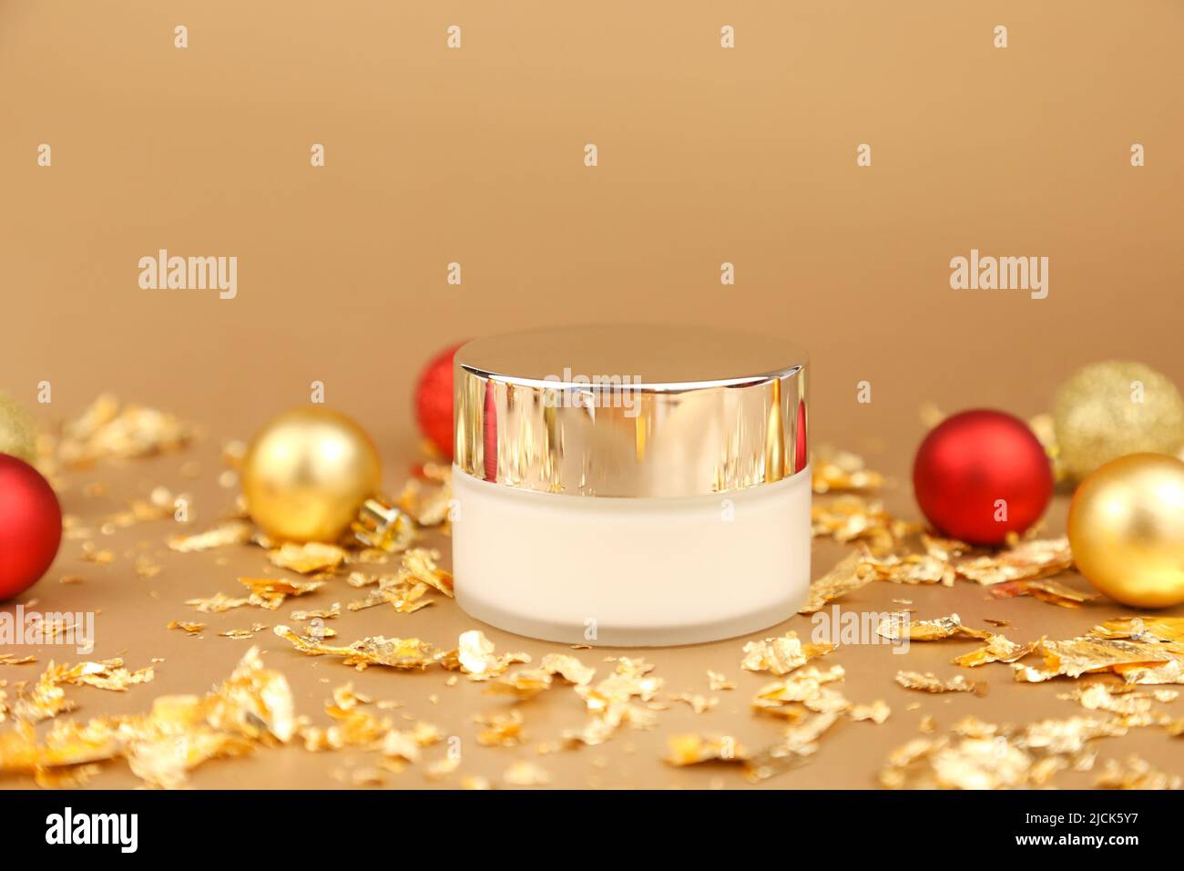 Unbranded jar of cream with metal mirror cap, red and gold christmas balls and pieces of gold paper firecracker on golden background. Luxurious antiag Stock Photo