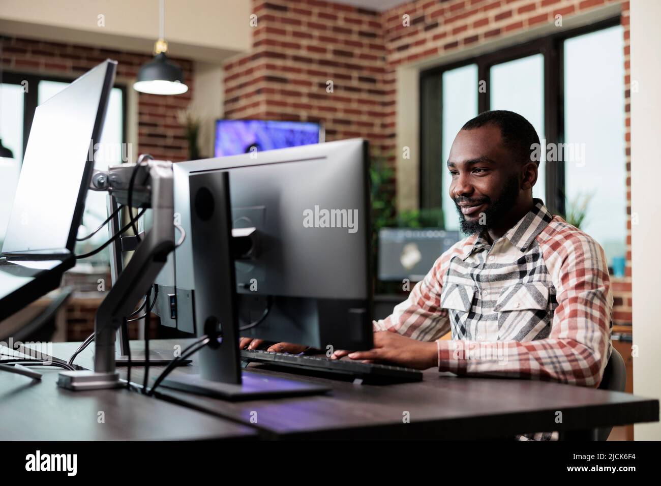 Confident creative office worker sitting at computer in office workspace while developing digital art. Professional employee graphics designer sitting at desk while working on project. Stock Photo
