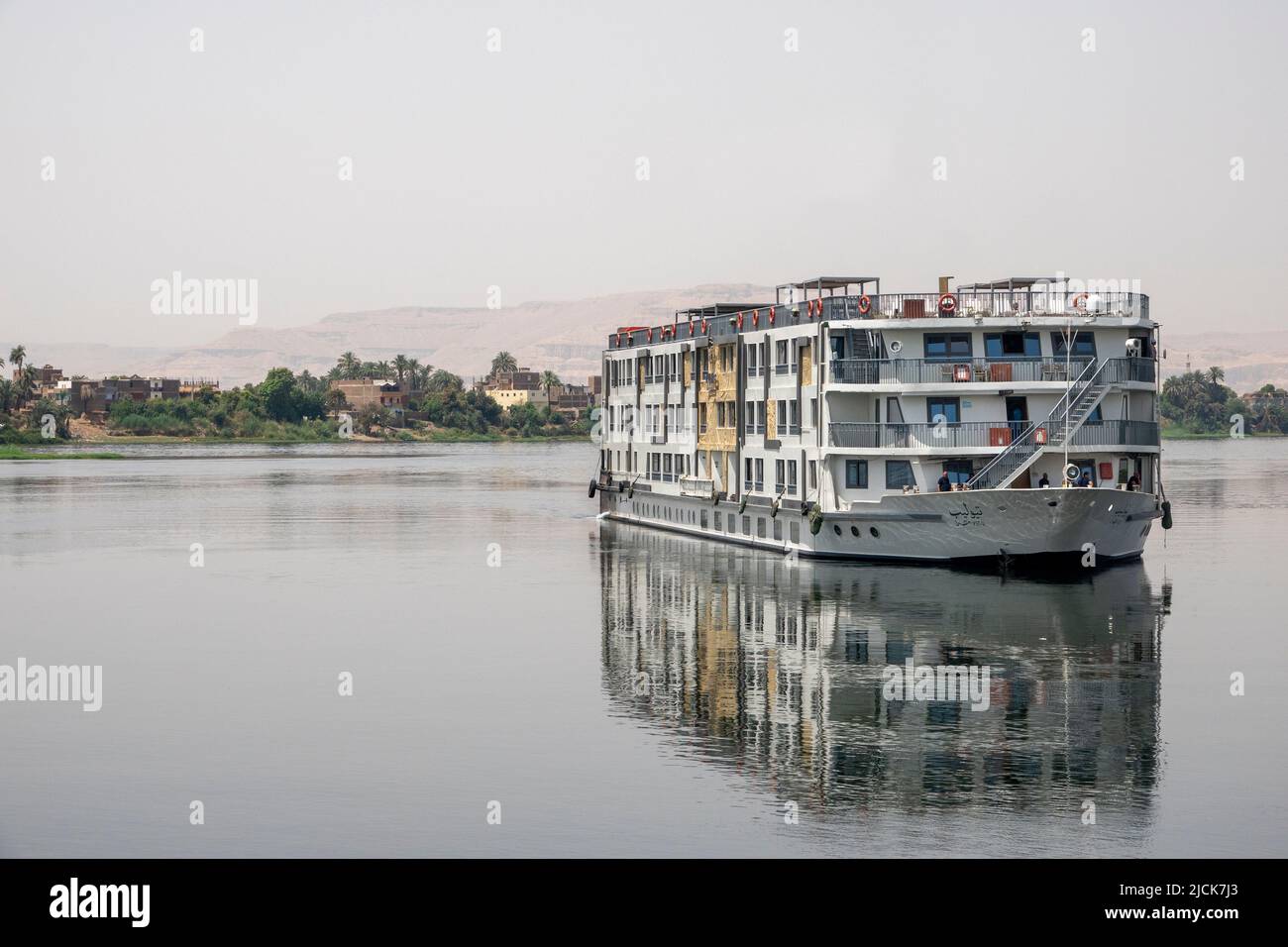 Nile cruise boat sailing at a 45% angle towards camera on calm water with reflections in early morning light Stock Photo