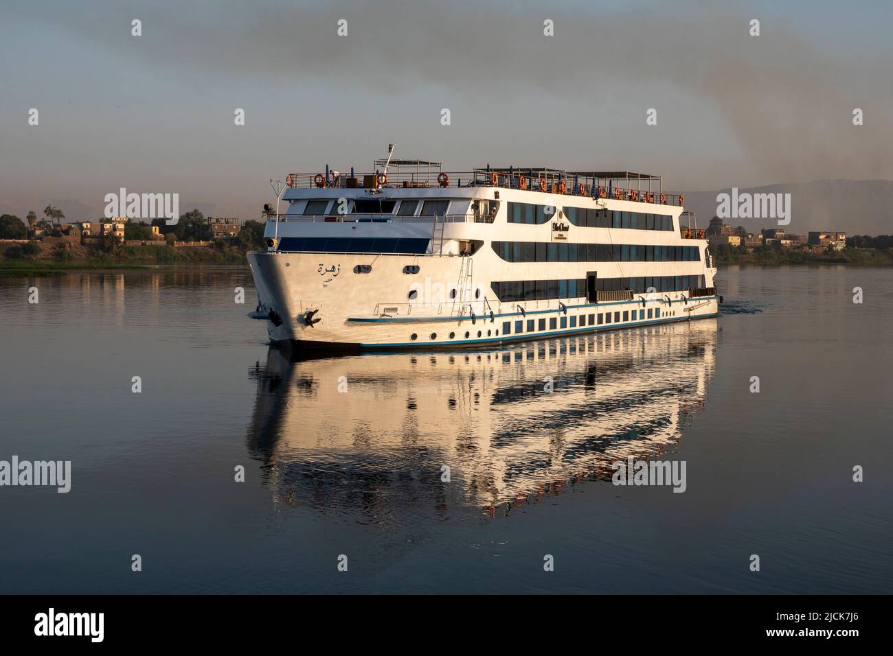 Nile cruise boat sailing on the calm water with reflections in early morning light Stock Photo