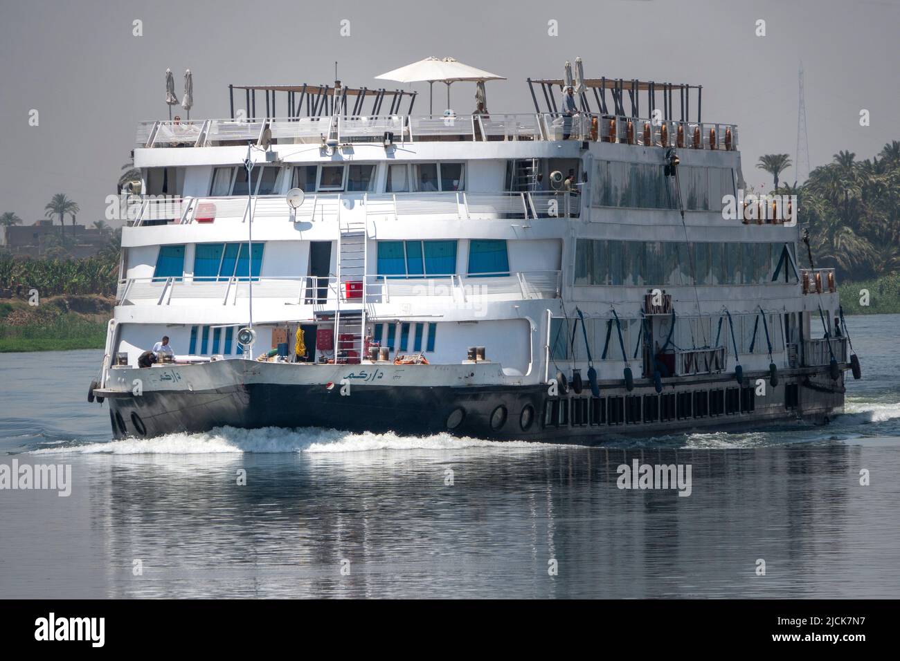 Nile cruise boat sailing 45% to camera on calm water with small white wake ahead with reflections in early morning light Stock Photo