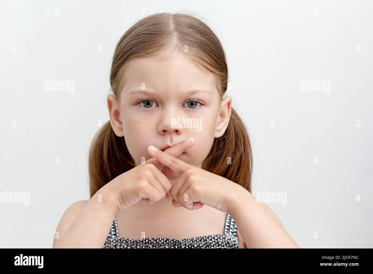 Caucasian serious little girl of 6 years crossed fingers on mouth showing speechless and voiceless Stock Photo