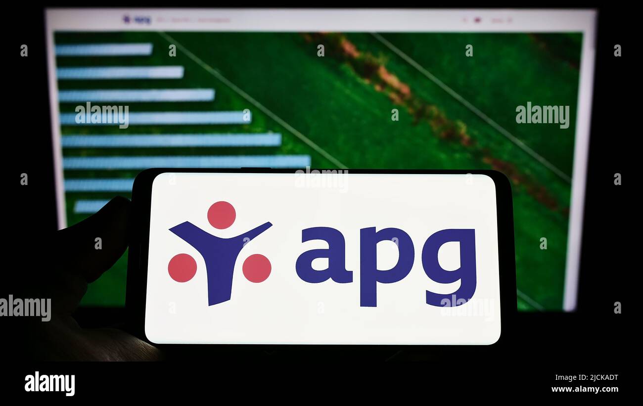 Person holding smartphone with logo of pension fund Algemene Pensioen Groep (APG) on screen in front of website. Focus on phone display. Stock Photo