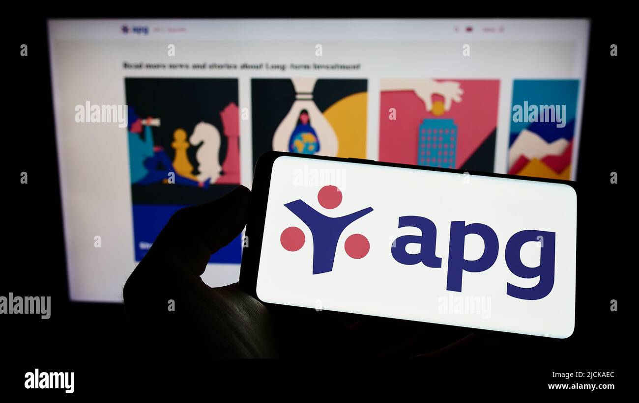 Person holding cellphone with logo of pension fund Algemene Pensioen Groep (APG) on screen in front of business webpage. Focus on phone display. Stock Photo