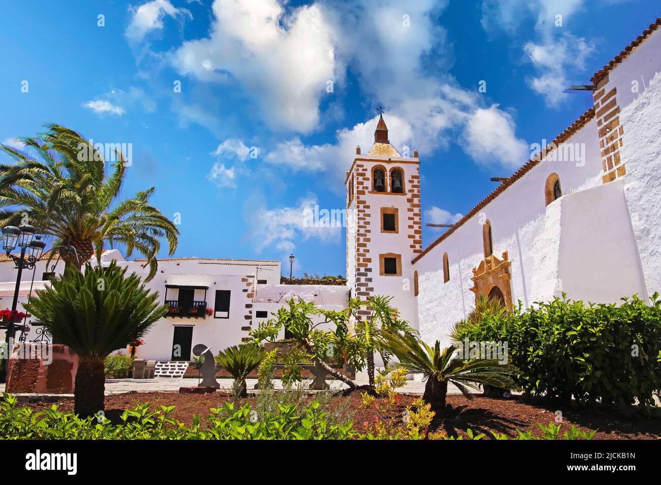Beautiful colonial canary island  style typical traditional church, white houses, bell tower, garden, palm tree, blue summer sky - Betancuria, Fuertev Stock Photo