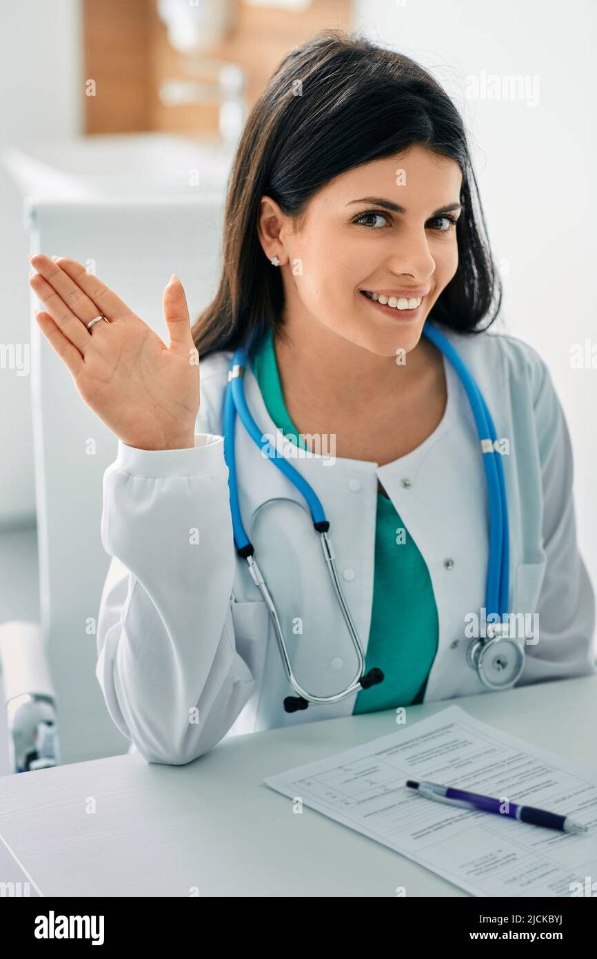 Smiling physician sitting at her workplace wearing medical uniform at hospital Stock Photo