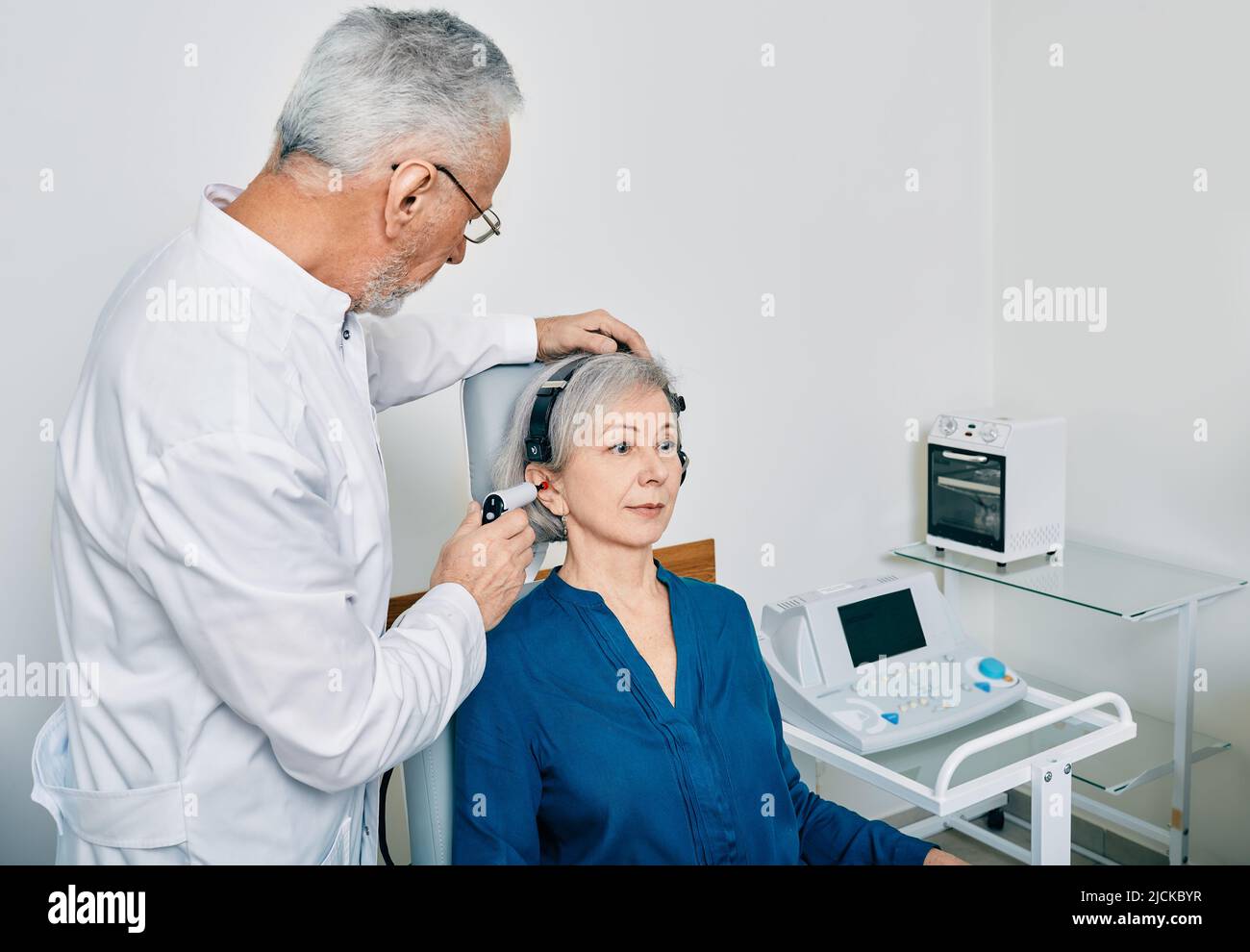 Mature audiologist with tympanometer probe doing procedure tympanometry or impedance audiometry for senior woman patient at hearing clinic Stock Photo