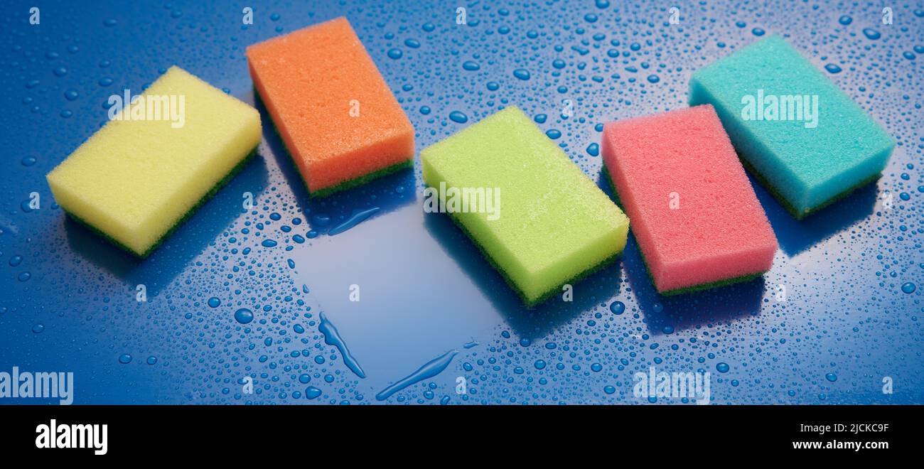 From above of various colorful sponges for dishwashing placed on wet blue background with water drops during household routine in room Stock Photo