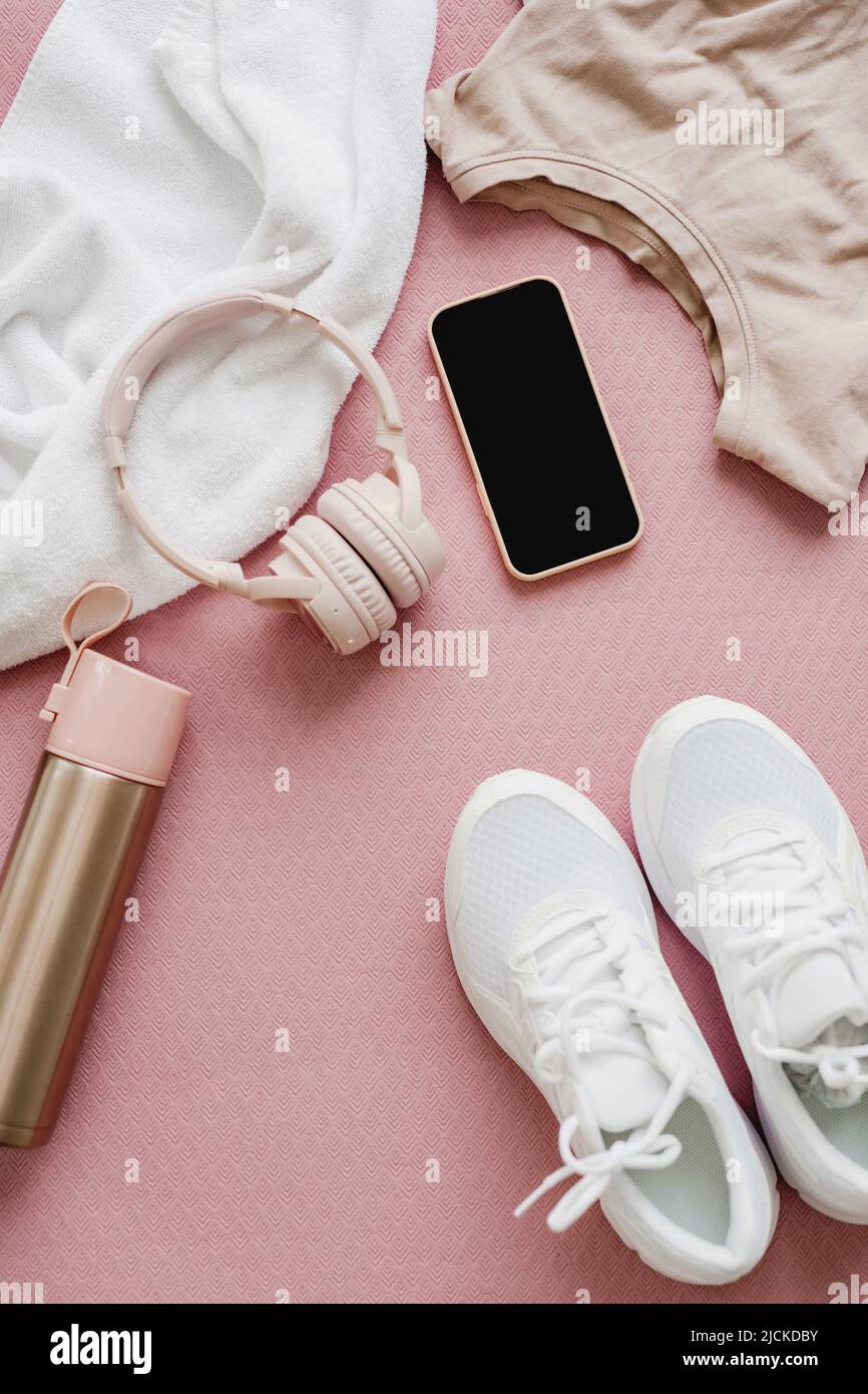 Flat lay of female sports clothing, smartphone, headphones, and a bottle of water on pink background. Stock Photo